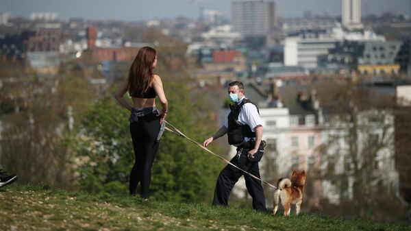 Полицейский в медицинской маске беседует с девушкой, выгуливающей собаку на Примроуз-Хилл Лондон, Великобритания